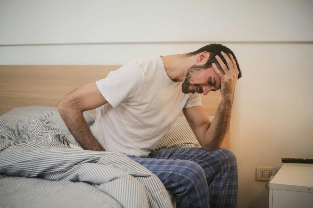 Man with head in hands at the end of the bed suffering from COVID-19